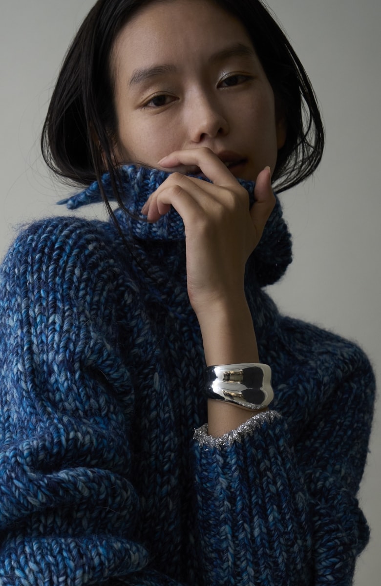 ブルーのハイネックのニットを着ている女性が口に手を当てて正面を向いている画像