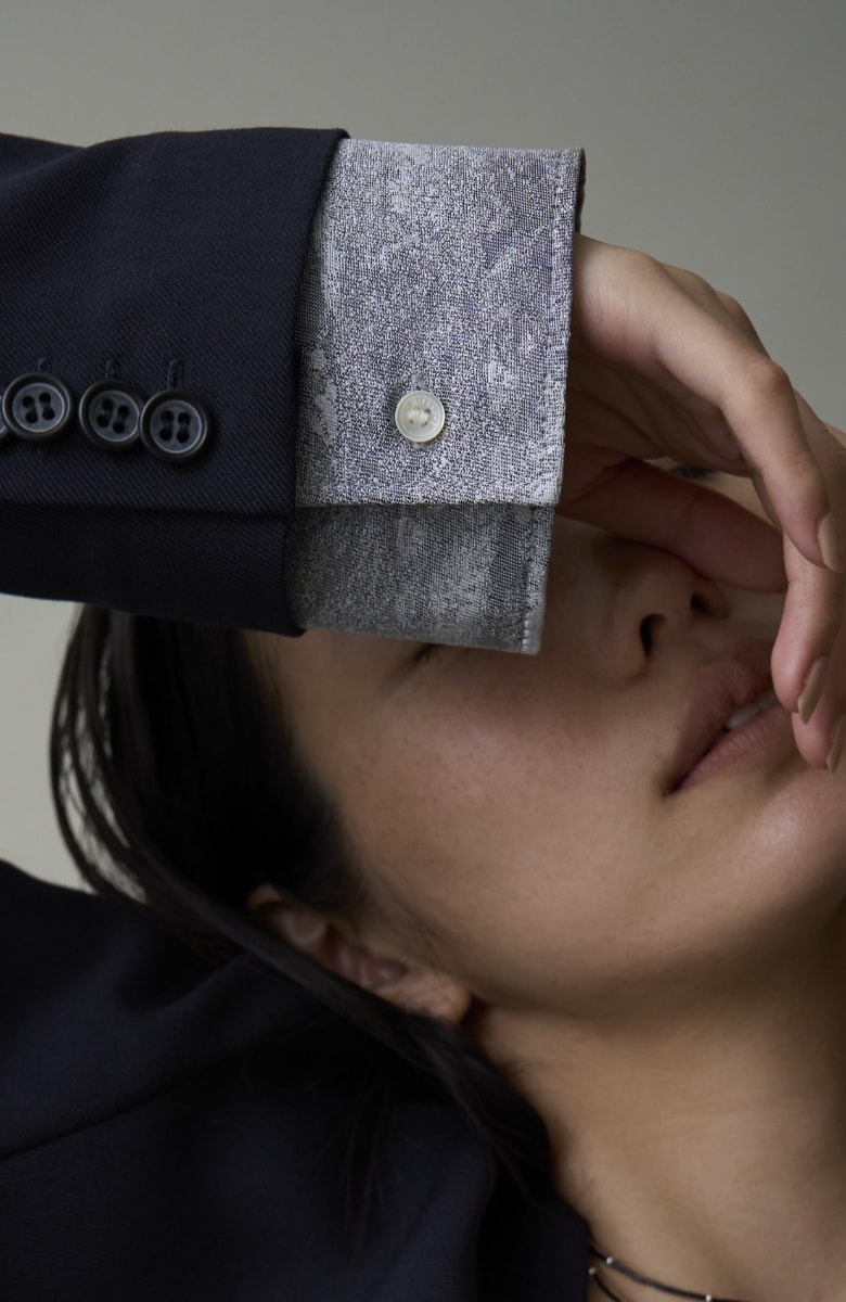 ネイビーのジャケットを着た女性が顔の前に手を当てている画像